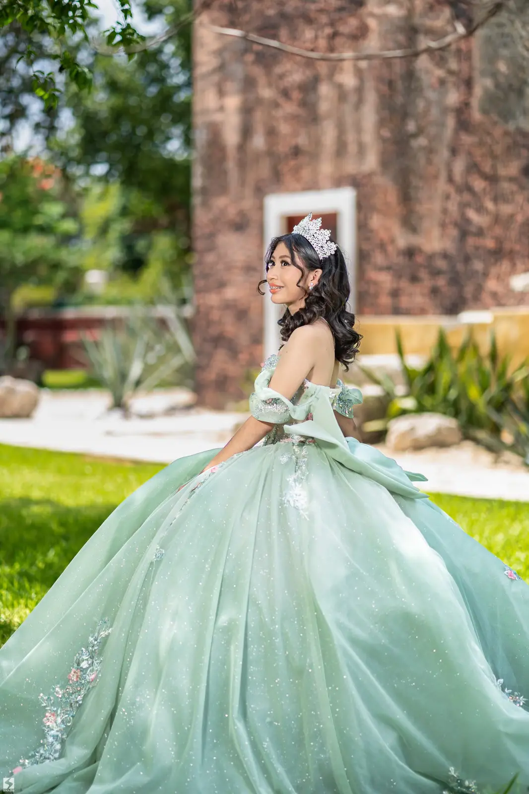 Quinceañera con vestido verde menta y corona en un jardín