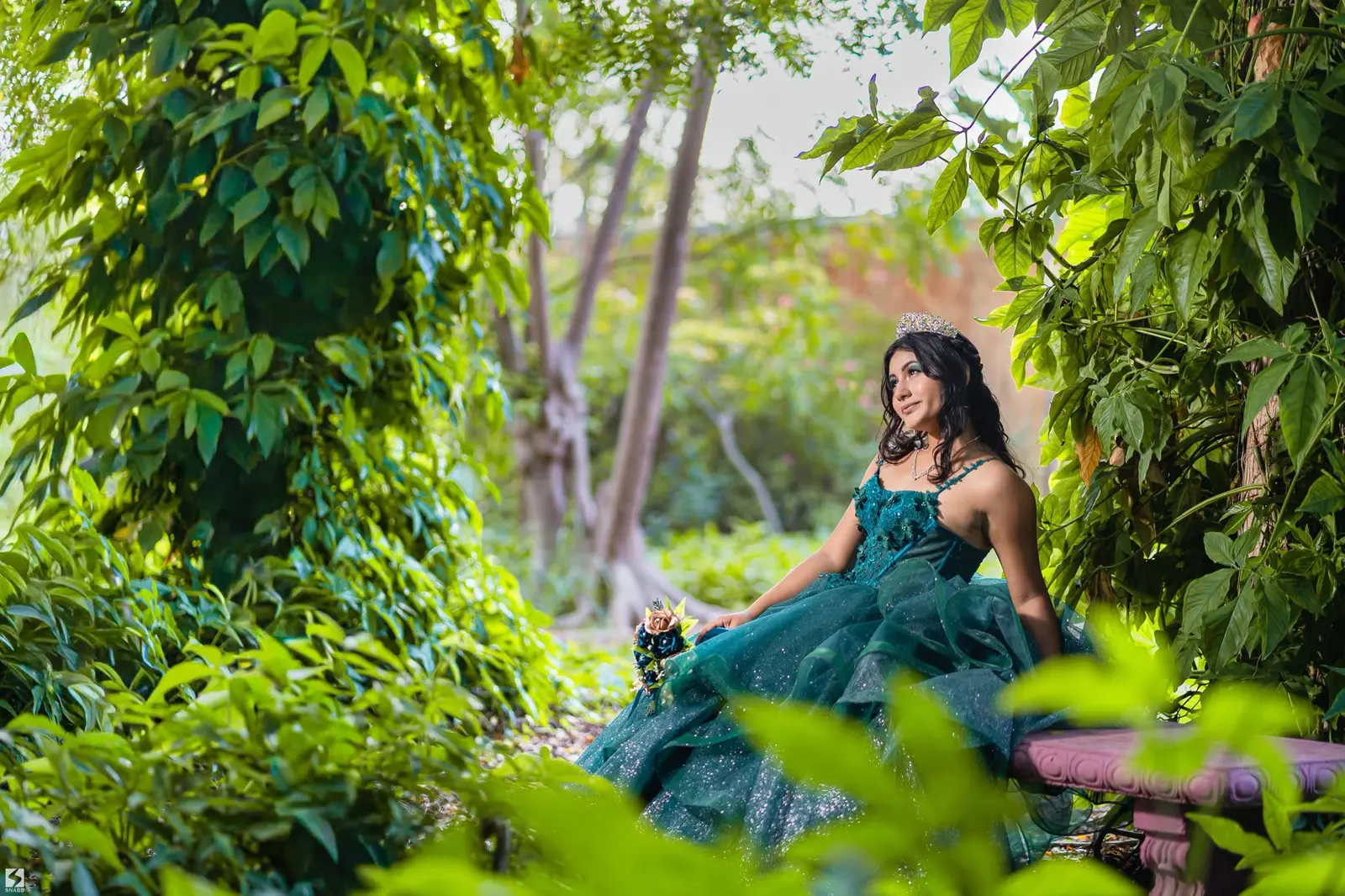 Quinceañera con vestido esmeralda entre la vegetación