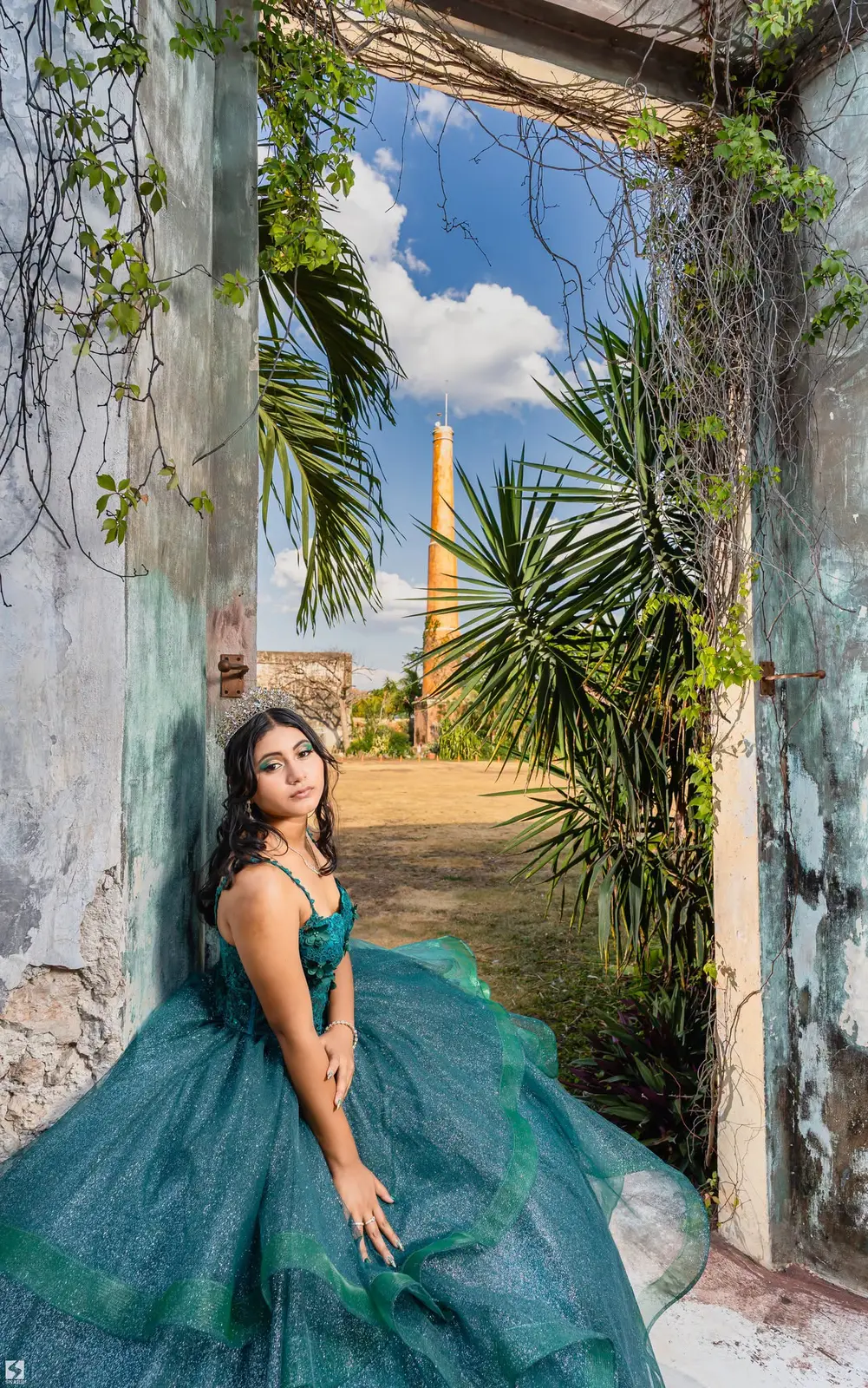Quinceañera con vestido verde esmeralda junto a un arco de piedra
